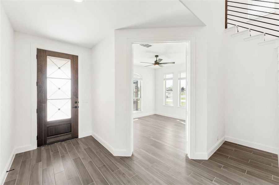 Entryway with dark wood front door, wood-look tile floors, and open view into living room with ceiling fan Entryway with dark wood front door, wood-look tile floors, and open view into living room with ceiling fan