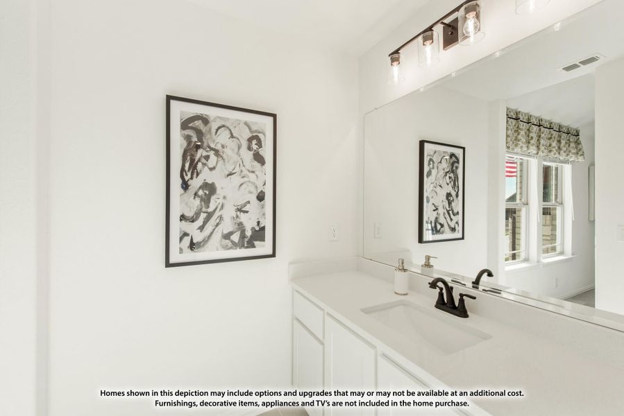 Bathroom vanity with white cabinets, light countertop, dark faucet, large mirror, and wall-mounted light fixture above. Bathroom vanity with white cabinets, light countertop, dark faucet, large mirror, and wall-mounted light fixture above.