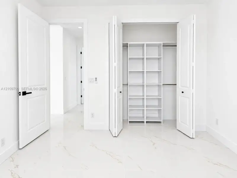 Polished stone-finish tile flooring, walk-in closet with built-in white shelving, and solid-core interior doors with matte black hardware