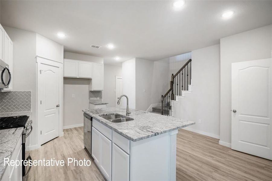 This open-concept kitchen features white cabinetry, stainless steel appliances, granite countertops, and a herringbone tile backsplash