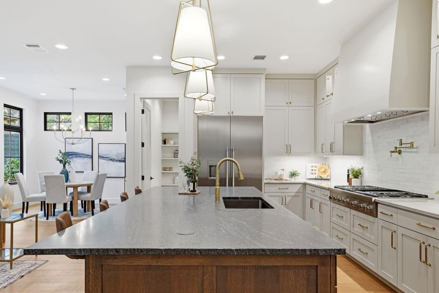 Kitchen featuring dark stone countertops, wall chimney range hood, a kitchen island with sink, and recessed lighting
