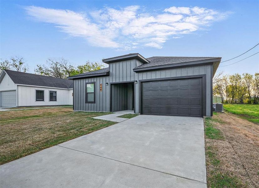 View of front of home with a garage, concrete driveway, a front yard, board and batten siding, and cooling unit View of front of home with a garage, concrete driveway, a front yard, board and batten siding, and cooling unit