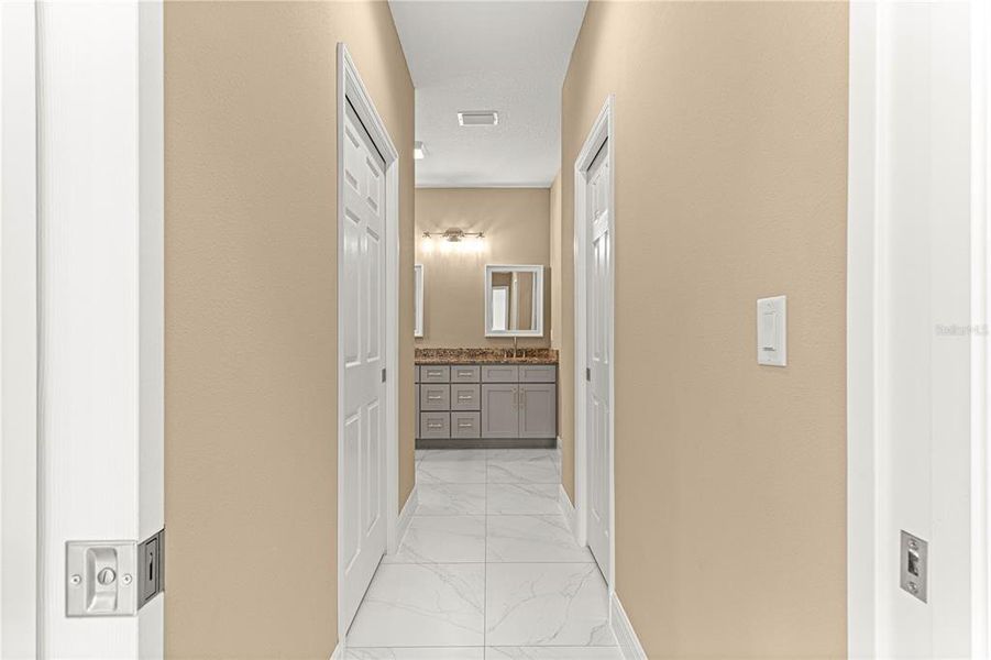 HALLWAY IN PRIMARY SUITE TO BATHROOM AREA WITH 1 LARGE WALK-IN CLOSET AND A SECONDARY CLOSET WITH POCKET DOORS