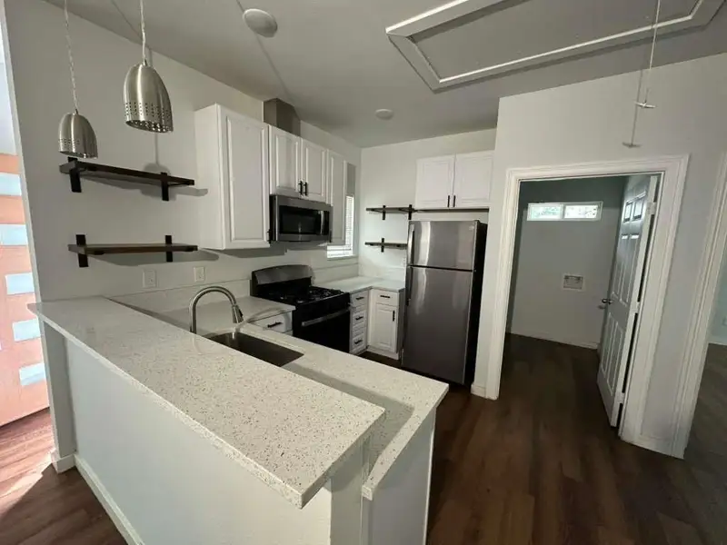 Kitchen featuring open shelves, stainless steel appliances, white cabinets, dark wood-style flooring, and a peninsula