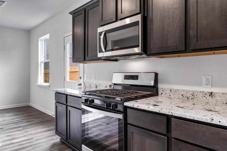 Kitchen with light stone countertops, dark brown cabinets, light hardwood / wood-style flooring, and stainless steel appliances