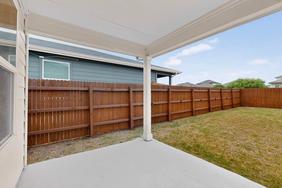 A covered back porch overlooks the fully fenced grassy backyard.