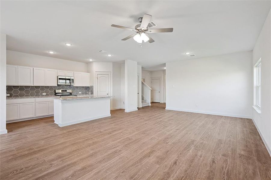 Kitchen featuring light wood-type flooring, white cabinets, stainless steel appliances, a center island with sink, and ceiling fan