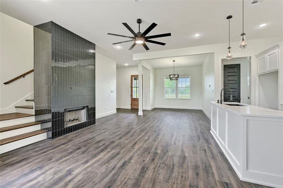 Unfurnished living room featuring a sink, ceiling fan with notable chandelier, stairs, baseboards, and dark wood-type flooring