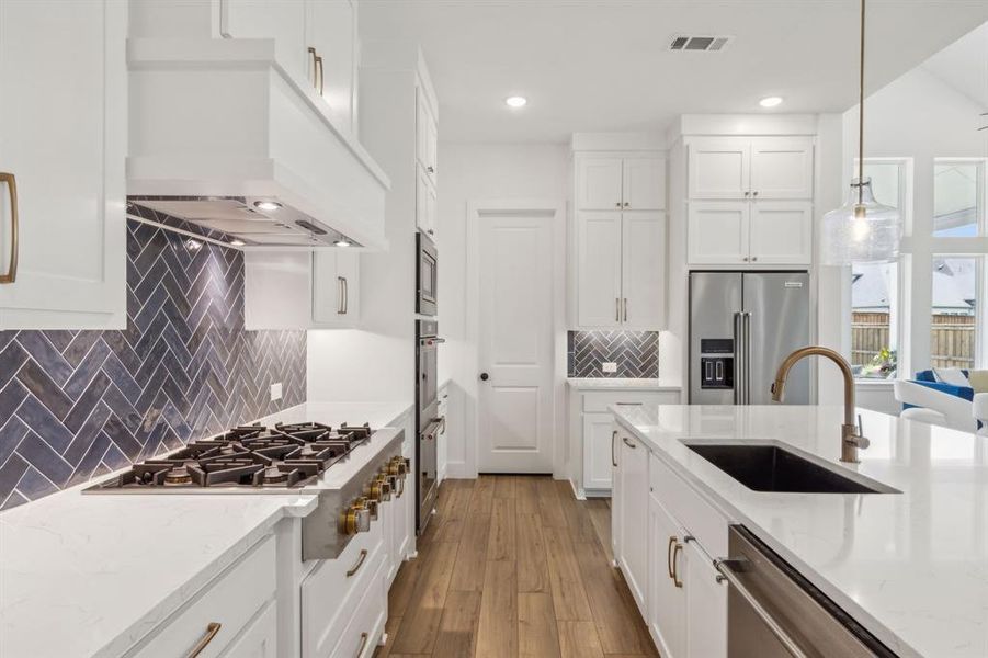 Kitchen with built in appliances, sink, hanging light fixtures, premium range hood, and decorative backsplash