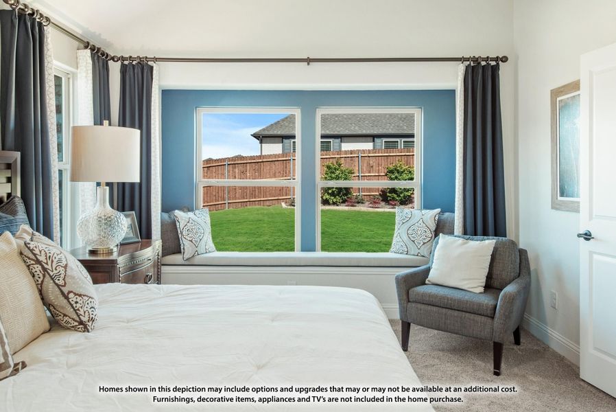 Bedroom with blue accent wall, built-in window seat, large windows overlooking fenced backyard, and gray accent chair