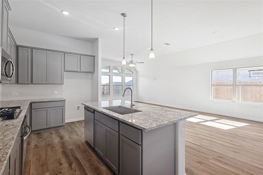 Kitchen featuring light stone countertops, sink, a kitchen island with sink, appliances with stainless steel finishes, and hardwood / wood-style flooring