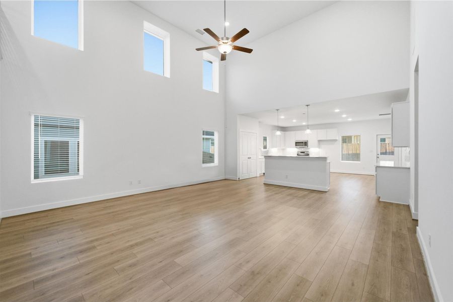 Unfurnished living room featuring a ceiling fan, a high ceiling, light wood-style floors, and recessed lighting