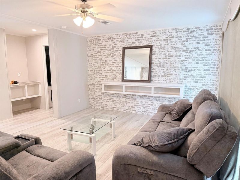 A relaxed living area with whitewashed brick-patterned walls and light wood-tone flooring offers a comforting retreat.