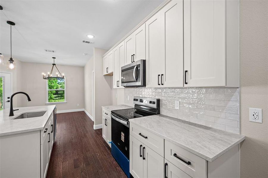 Kitchen featuring white shaker cabinetry with black hardware, stainless steel appliances, light-toned countertops, and wood-finish flooring
