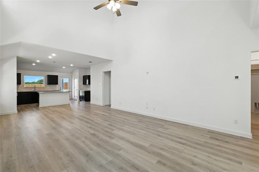 Unfurnished living room featuring a high ceiling, ceiling fan, a fireplace, recessed lighting, and light wood-style floors Unfurnished living room featuring a high ceiling, ceiling fan, a fireplace, recessed lighting, and light wood-style floors