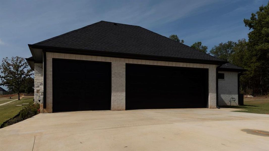 View of property exterior with a shingled roof, a garage, brick siding, an outdoor structure, and driveway View of property exterior with a shingled roof, a garage, brick siding, an outdoor structure, and driveway