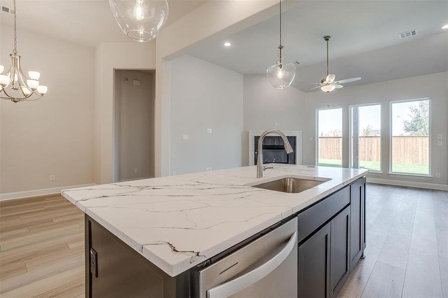 Kitchen with dishwasher, sink, light stone counters, light hardwood / wood-style floors, and a kitchen island with sink