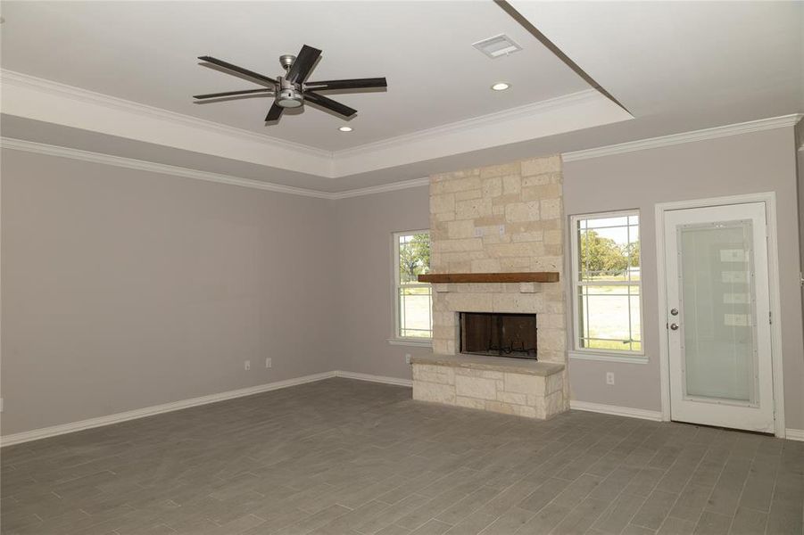 Living room featuring a tray ceiling, ornamental molding, a stone fireplace, and ceiling fan