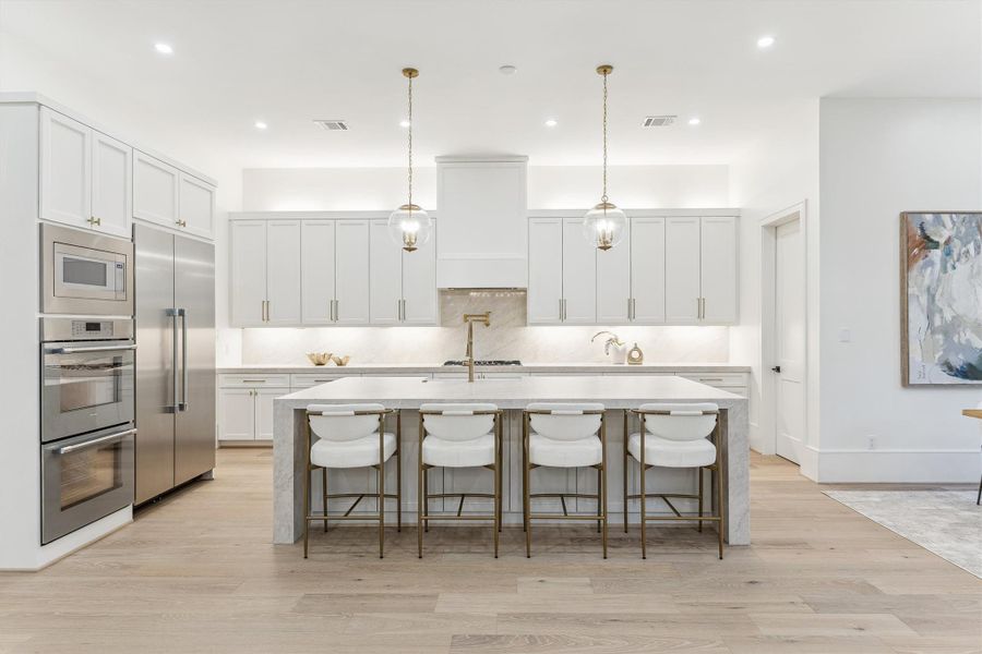 The kitchen features stunning Taj Mahal quartzite countertops and a waterfall-edge island, complemented by glamorous pendant lighting.