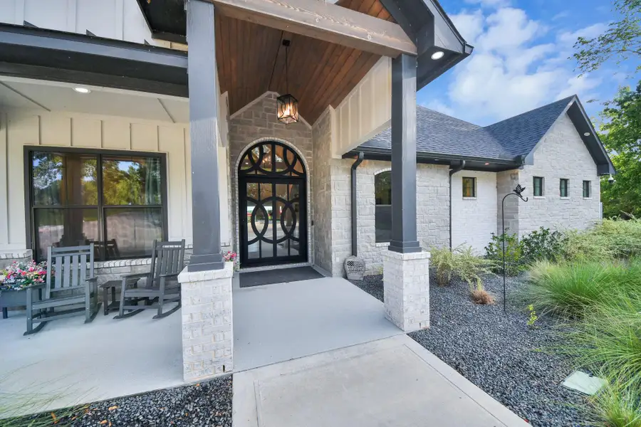 Charming entryway with a modern arch door and inviting porch, accented by elegant stonework and lush landscaping.