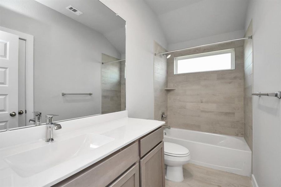 Secondary bath features tile flooring, bath/shower combo with tile surround, light stained wood cabinets, beautiful light countertop.  Sample photo of completed home with similar floor plan. Actual colors and selections may vary.