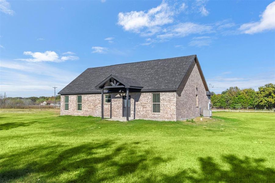 View of front of home with a front yard, a patio, brick siding, and a shingled roof