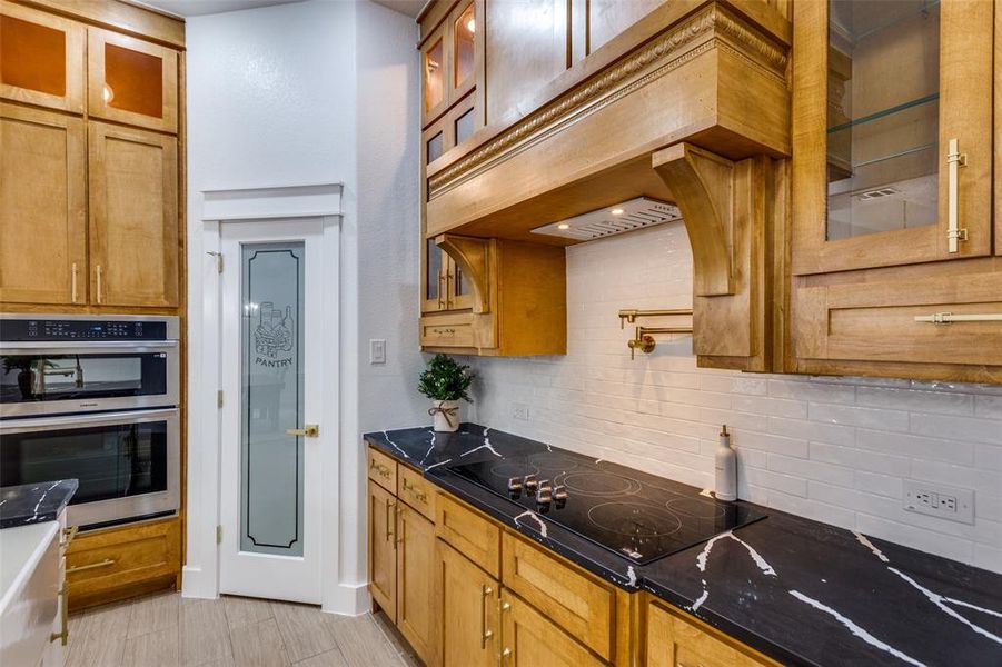 Kitchen featuring tasteful backsplash, dark stone countertops, black electric stovetop, and double oven