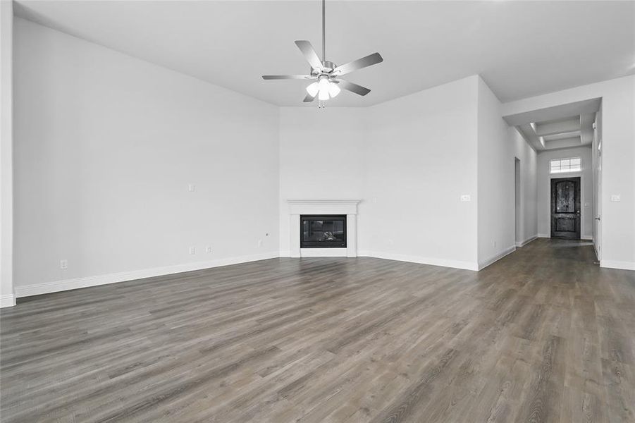 Unfurnished living room featuring a glass covered fireplace, baseboards, ceiling fan, and wood finished floors