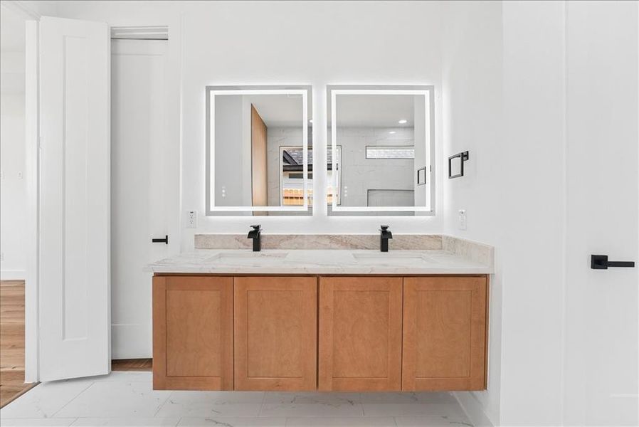 Dual illuminated vanity mirrors over a wood-finish floating vanity with a light-toned countertop, integrated sinks, and matte black fixtures Dual illuminated vanity mirrors over a wood-finish floating vanity with a light-toned countertop, integrated sinks, and matte black fixtures