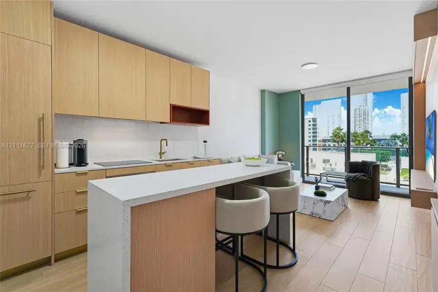 Kitchen featuring light wood-finish cabinetry, quartz countertops, a flat-panel peninsula, integrated appliances, and floor-to-ceiling glass sliding doors