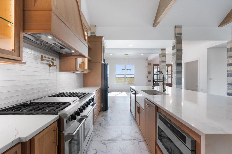 Kitchen with appliances with stainless steel finishes, light stone countertops, decorative backsplash, custom exhaust hood, and light marble finish flooring