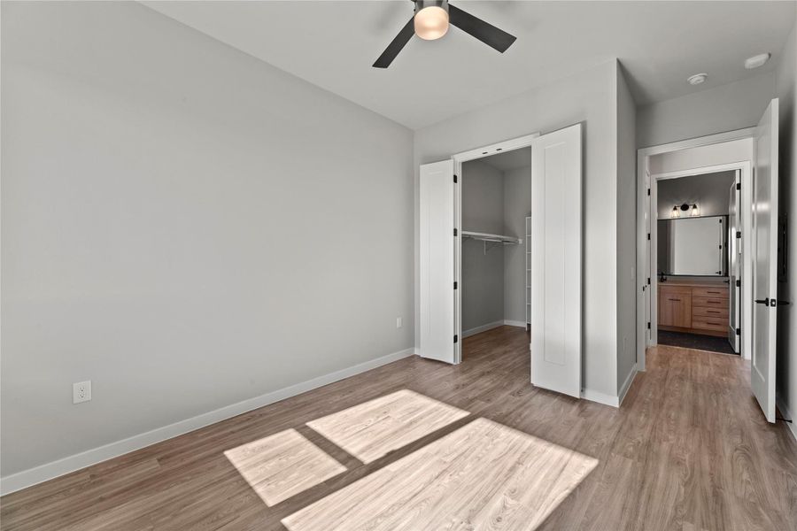 Unfurnished bedroom featuring ceiling fan, a walk in closet, a closet, and light hardwood / wood-style flooring