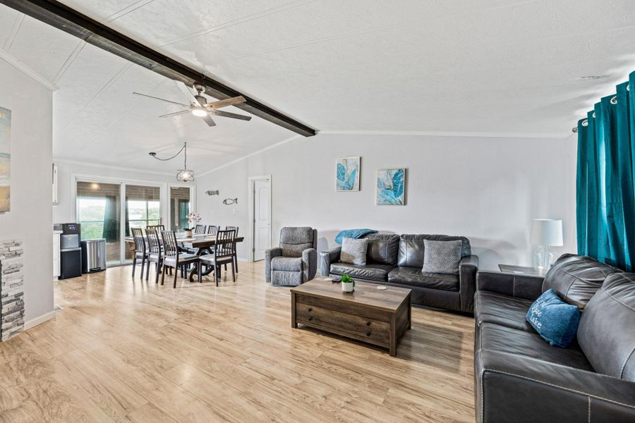 Open-concept living space featuring wood-finish flooring, a decorative ceiling beam, and a ceiling fan with integrated lighting