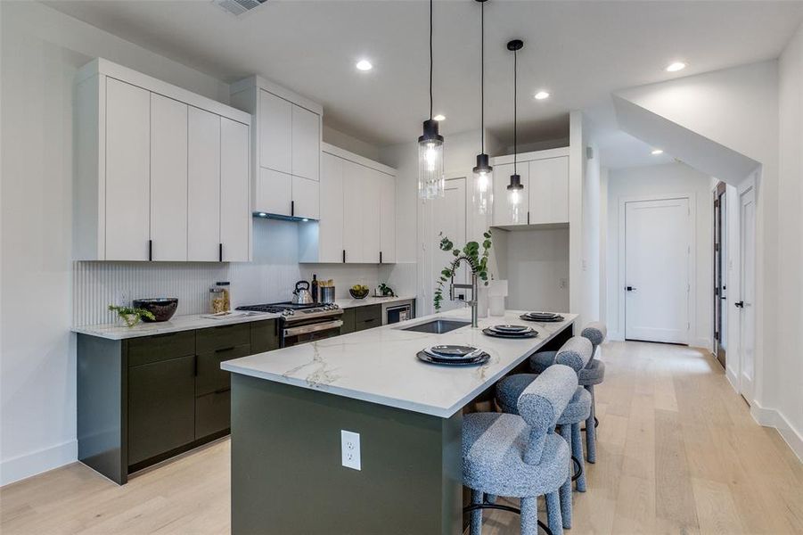 Kitchen with sink, a kitchen island with sink, white cabinetry, hanging light fixtures, and stainless steel range with gas cooktop