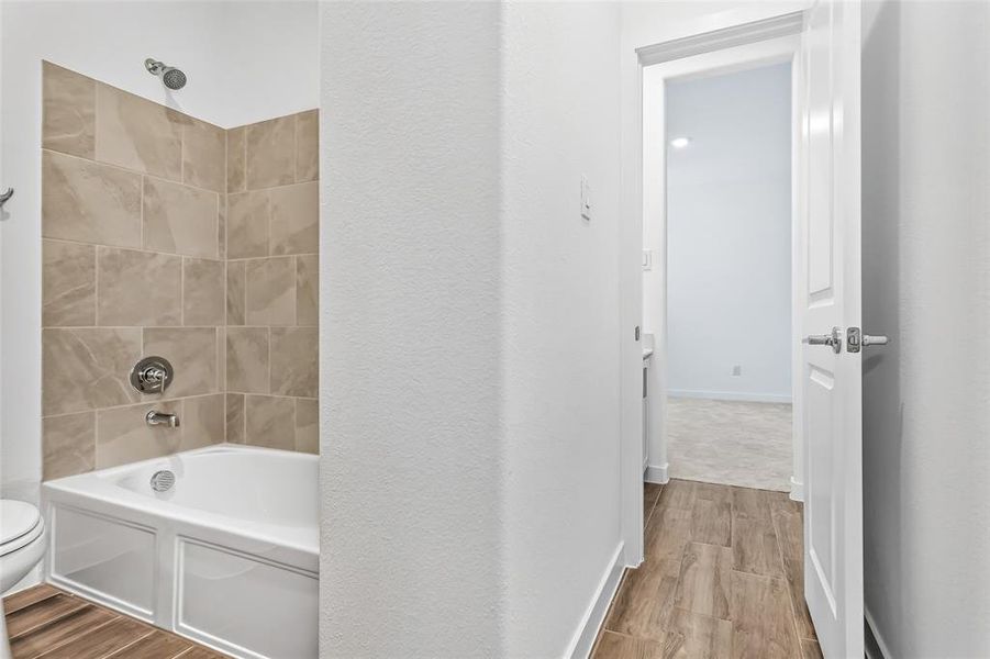 Jack and Jill bathroom featuring a white tub with chrome fixtures and tan subway tile surround, wood-finish flooring, and a white interior door. Private sink areas.