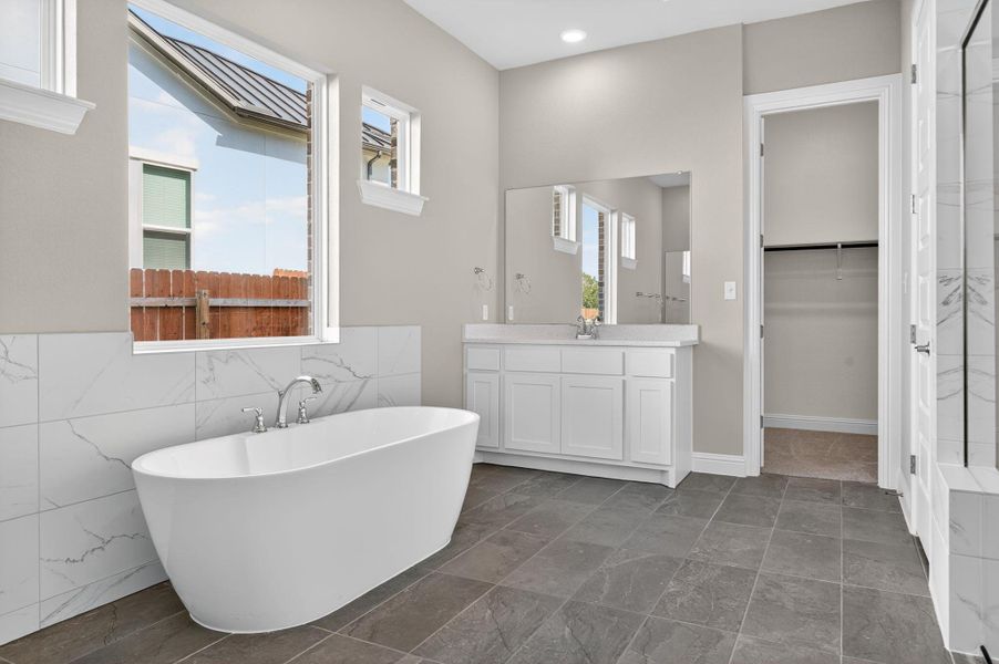 Full bath with a soaking tub, vanity, a spacious closet, and tile walls