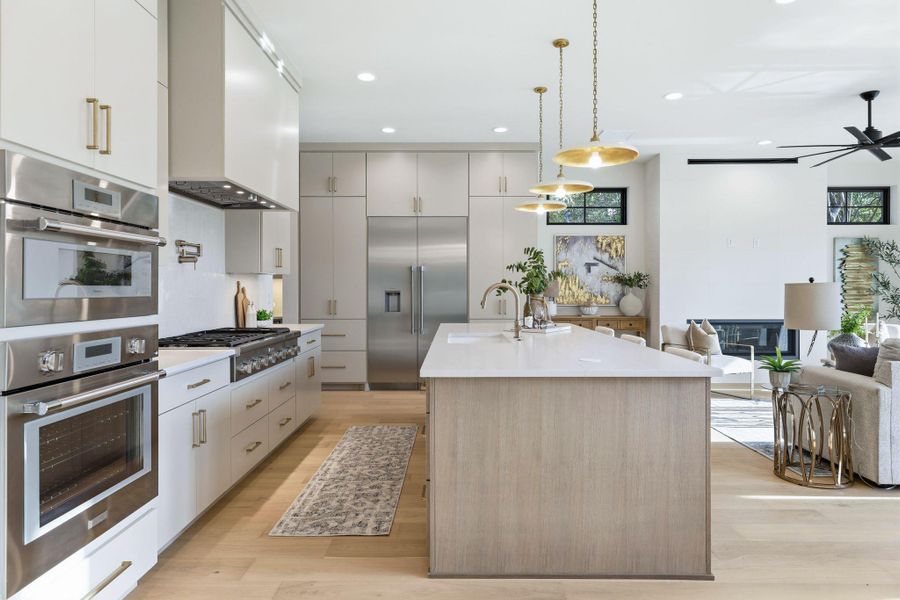 Kitchen featuring stainless steel appliances, open floor plan, an island with sink, pendant lighting, and light wood-style floors