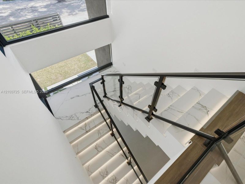 Staircase featuring stone-finish treads, glass railings with metal posts, integrated tread lighting, and a multi-level window installation