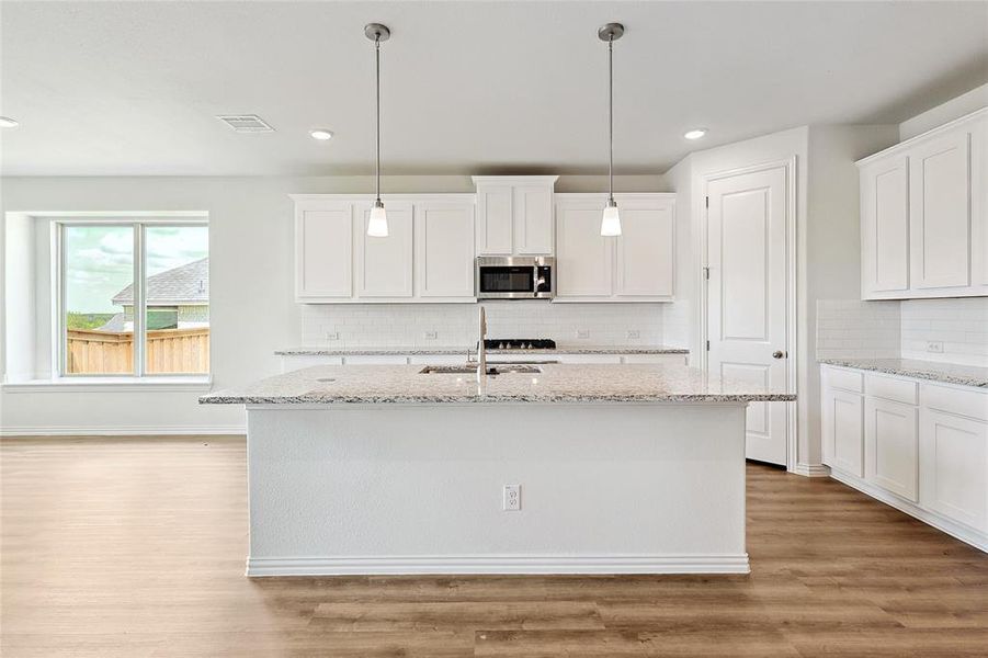 Kitchen with an island with sink, white cabinets, hanging light fixtures, light hardwood / wood-style flooring, and backsplash