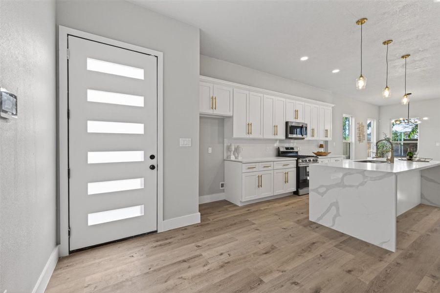 Sun-filled entry opens to an expansive open-concept layout featuring white oak–toned plank laminate flooring, smooth contemporary walls, and a modern frosted-glass front door that balances privacy with natural light.