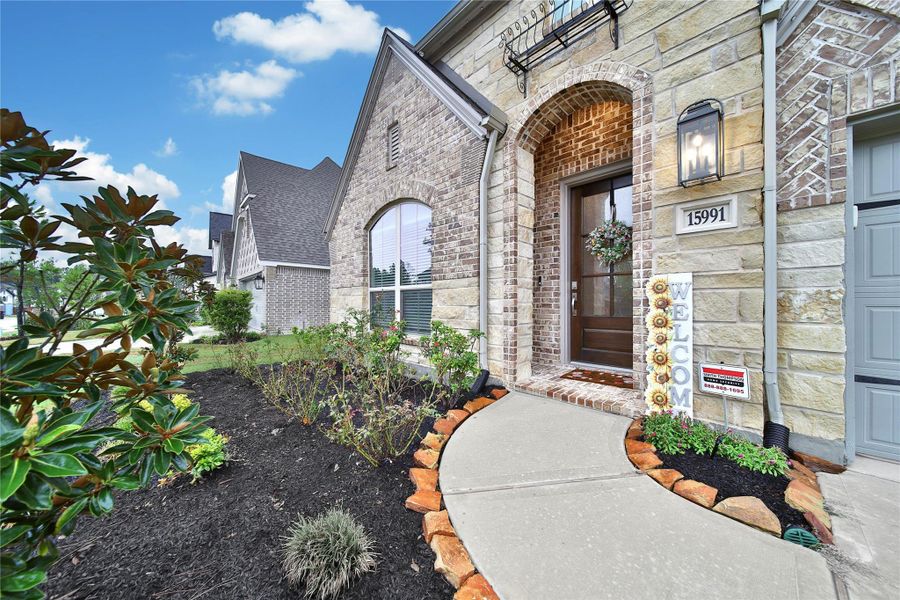 Brick & stone detailing gives the front elevation timeless appeal, complemented by a classic wood door with glass panels. The artisan metal accent, coach light, gutters & beautifully landscaped flower beds complete the stunning exterior.
