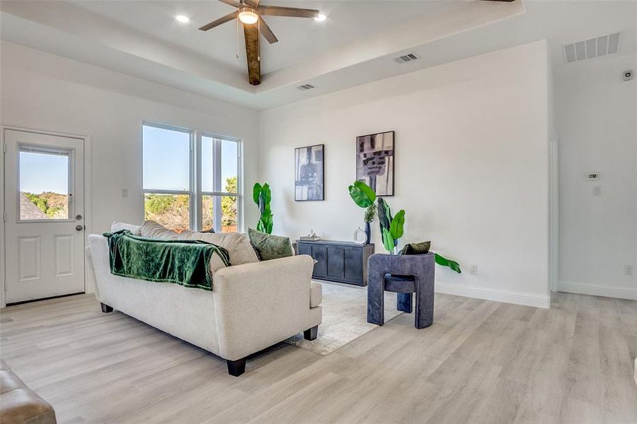 Living area with a raised ceiling, light wood-style flooring, and ceiling fan Living area with a raised ceiling, light wood-style flooring, and ceiling fan