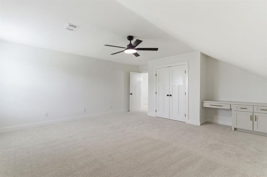Spacious room featuring light-colored carpeting, a ceiling fan with integrated lighting, and built-in cabinetry with a desk area Spacious room featuring light-colored carpeting, a ceiling fan with integrated lighting, and built-in cabinetry with a desk area