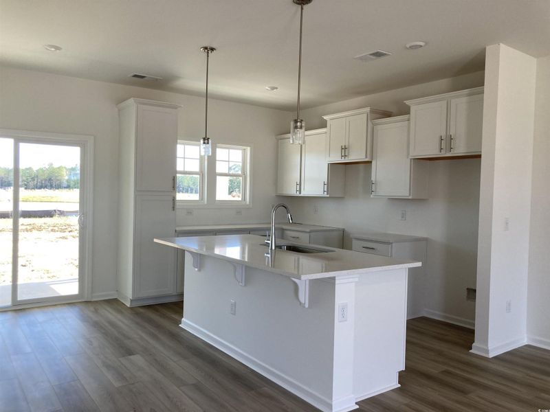 Kitchen with white cabinets, dark wood finished floors, hanging light fixtures, a breakfast bar area, and light stone countertops