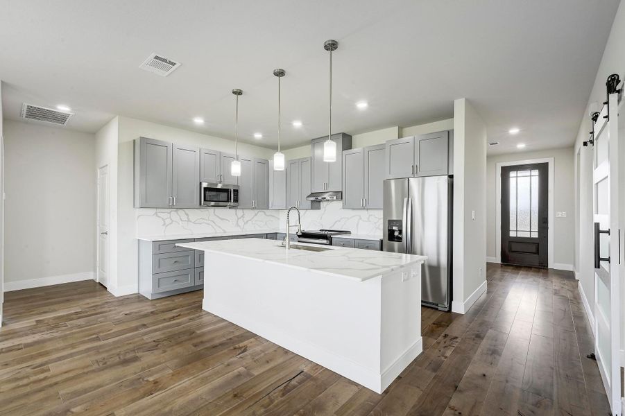 Kitchen featuring appliances with stainless steel finishes, a barn door, gray cabinets, tasteful backsplash, and light stone counters