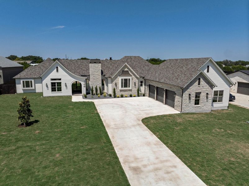 French country home with stone siding, concrete driveway, a front yard, a garage, and a chimney