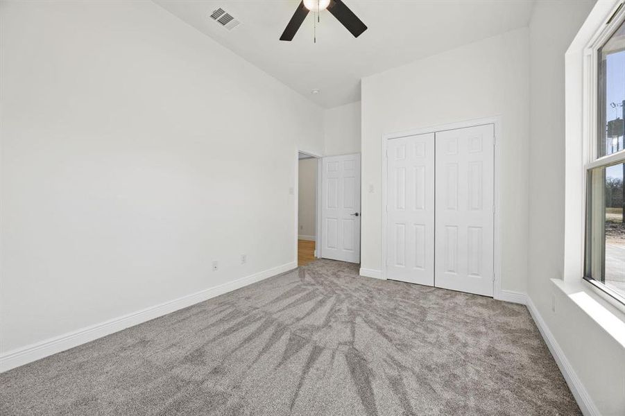 Carpeted room featuring a ceiling fan with light, white trim, a double-panel closet door, and a single-pane window Carpeted room featuring a ceiling fan with light, white trim, a double-panel closet door, and a single-pane window