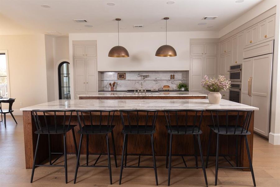 Kitchen featuring light wood-style flooring, light stone countertops, hanging light fixtures, a kitchen bar, and paneled refrigerator