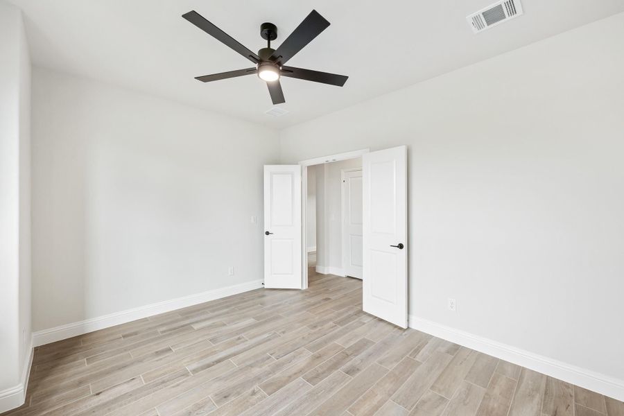 Empty bedroom with light wood floors, white walls, black ceiling fan, and two open doors
