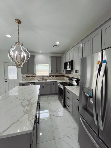 Kitchen with tasteful backsplash, appliances with stainless steel finishes, gray cabinets, and a notable chandelier Kitchen with tasteful backsplash, appliances with stainless steel finishes, gray cabinets, and a notable chandelier
